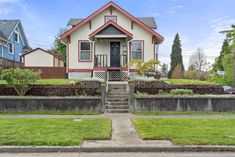 a small house on the corner of a street with grass and bushes in front of it