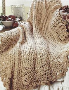 a crocheted blanket sitting on top of a bed next to a bowl of fruit