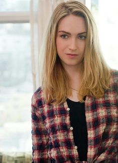 a woman with long blonde hair wearing a plaid shirt and black top standing in front of a window