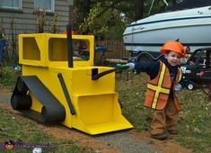 a young boy dressed as a construction worker standing next to a yellow bulldozer