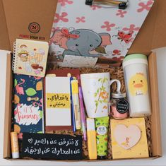 an open box containing various items such as pens, notebooks, and coffee cups