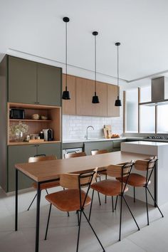 a kitchen with an island table surrounded by wooden chairs and black pendant lights hanging from the ceiling