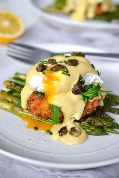 a white plate topped with asparagus and meat covered in hollandaise sauce