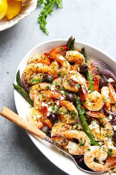 a white bowl filled with shrimp, asparagus and olives on top of a table