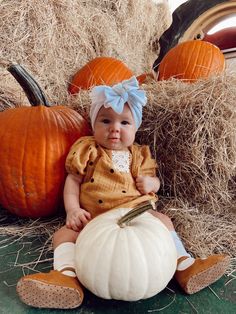 a baby sitting on hay next to pumpkins