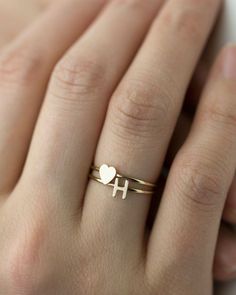 a woman's hand wearing a gold ring with a heart and cross on it