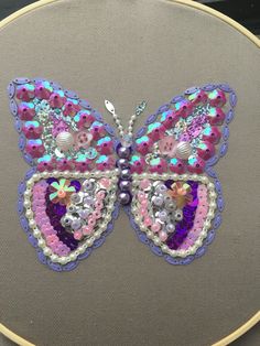 a colorful butterfly made out of sequins and beads on a gray surface with a circular frame