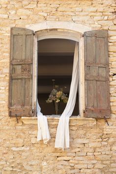 an open window with curtains and flowers in it