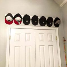 five hats are hanging on the wall above two white doors and three baseball caps hang from the ceiling