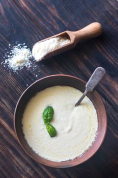 a bowl filled with soup next to a spoon and some salt on top of a wooden table