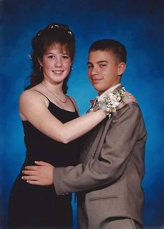 a young man and woman are posing for a photo in formal dress clothes, with their arms around each other's shoulders