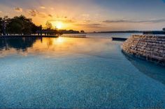 the sun is setting over an empty swimming pool in front of some trees and water