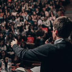 a man standing in front of a crowd holding a microphone and giving a speech to an audience