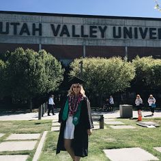 a woman is standing in front of the utah valley university building with her graduation cap on