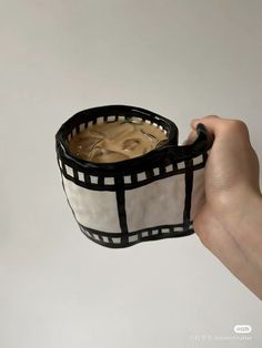 a hand holding a black and white cup filled with liquid in it's sleeve