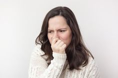 a woman covers her mouth with one hand while looking at the camera, against a white background