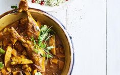 a bowl filled with meat and vegetables on top of a white table next to a spoon