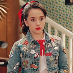 a woman wearing a jean jacket with patches on it and a red bow in her hair