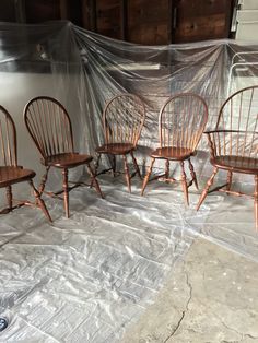 four wooden chairs sitting on top of a tarp covered floor next to a wall