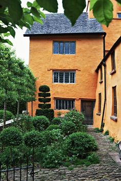 an orange building with trees and bushes around it's perimeter, in front of a stone path