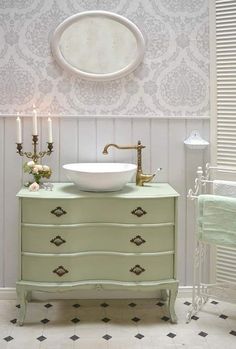 a white sink sitting on top of a green dresser next to a wall mounted mirror