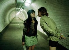 two people standing in a tunnel with one woman touching the other's face and looking at each other