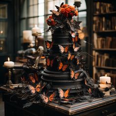 a table topped with a cake covered in butterflies next to candles and bookshelves