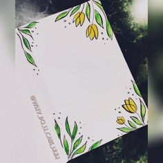 an open notebook with flowers and leaves on the cover is sitting in front of some trees