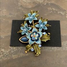 a blue flower brooch sitting on top of a black piece of paper with gold trim