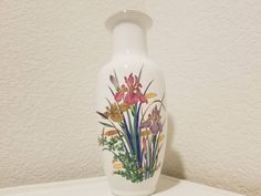 a white vase sitting on top of a table with flowers painted on the front and sides