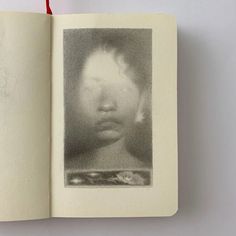 an open book with a drawing of a child's face on the page and red string attached to it