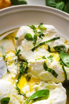 a white bowl filled with green vegetables and mozzarella cheese on top of it