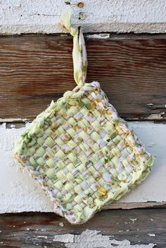 a woven square ornament hanging from a wooden wall with white paint and green fabric