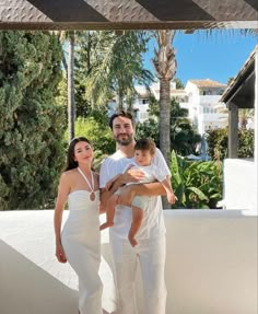 a man, woman and child standing on a balcony with palm trees in the background