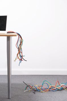 a laptop computer sitting on top of a wooden table covered in colorful wires and cords