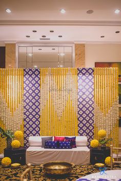 a living room filled with furniture and yellow drapes on the wall behind it is a white couch covered in colorful pillows