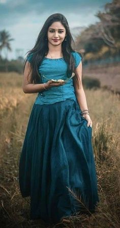 a woman in a blue dress holding a plate with food on it and standing in a field