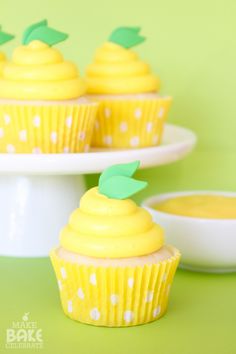 cupcakes with yellow frosting and green leaves on top are sitting on plates