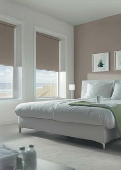 a white bed sitting in a bedroom next to two windows with blinds on each side