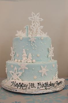 a blue and white cake with snowflakes on it's sides that says happy 1st birthday you