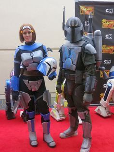 two people in costumes standing on a red carpet next to each other and one person wearing a helmet