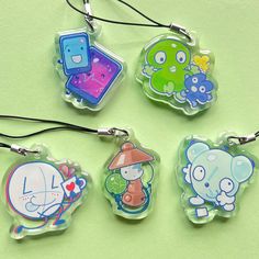 four keychains with cartoon characters on them sitting on a green surface and one has a cord attached to it