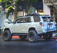 a light blue four door suv parked in front of a building with large tires on it