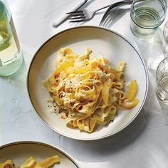 two plates with pasta and cheese on them next to wine glasses, silverware and utensils