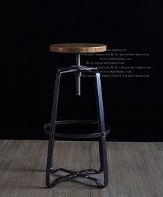 an industrial style bar stool with wooden seat and metal frame, in front of a black background