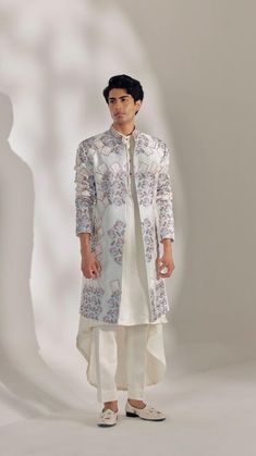 a man standing in front of a white background wearing a long coat and pants with floral designs on it