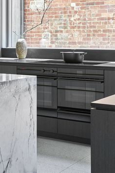 a kitchen with black cabinets and marble counter tops, along with a large window looking out onto the street