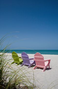 two lawn chairs sitting on top of a sandy beach