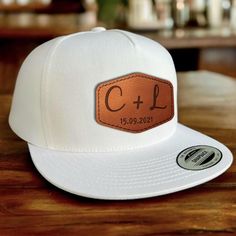 a white trucker hat with a leather patch on the front that says c + l