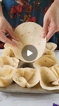 a woman is making tortillas on a tray with flowers in the background and a video about how to make tortilla shells